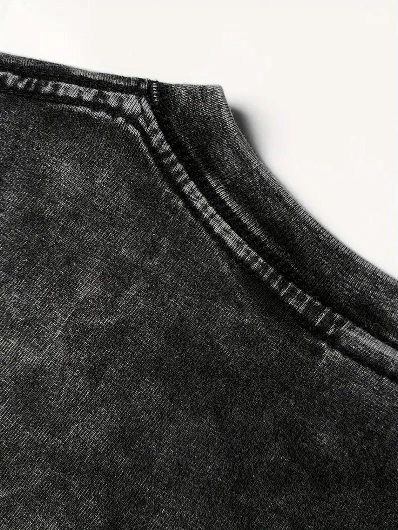 K&ouml;nnte beinhalten: Nahaufnahme des Ausschnitts eines schwarzen T-Shirts mit einem abgenutzten, verblassten Look. Der Stoff hat eine strukturierte, abgenutzte Optik.
