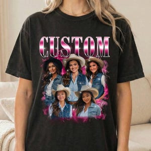 Puede incluir: Una camiseta negra de manga corta con la palabra CUSTOM en grandes letras metálicas rosas en la parte superior. Debajo del texto hay un collage gráfico de cuatro personas con chalecos vaqueros y sombreros de vaquero, rodeadas de rayos rosas.