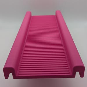 May include: Pink plastic pet ramp with a textured surface. The ramp has rounded edges and a slight curve.