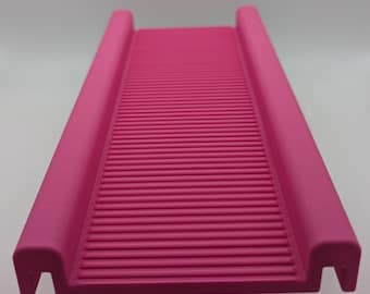 Può includere: Una rampa rettangolare rosa brillante caratterizzata da una superficie testurizzata con creste orizzontali e binari laterali rialzati. L'oggetto presenta un ritaglio a forma di U su ogni angolo della base, offrendo una struttura stabile.