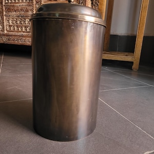 Peut inclure: Un grand récipient cylindrique en métal avec un couvercle. Le récipient a une finition bronze et un dessus arrondi avec une petite poignée. Le récipient est probablement utilisé pour le stockage ou comme objet décoratif.