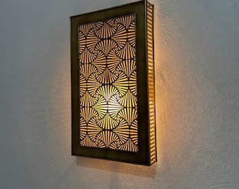 May include: Rectangular wall sconce with a geometric pattern. The sconce has a dark bronze frame and a patterned interior that emits a warm, inviting light. The design features a series of radiating lines and shapes, creating a visually appealing effect.