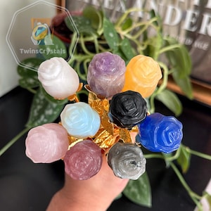 May include: A bouquet of nine rose-shaped crystal flowers with gold stems. The roses are carved from various gemstones, including amethyst, rose quartz, clear quartz, blue lace agate, and black obsidian.