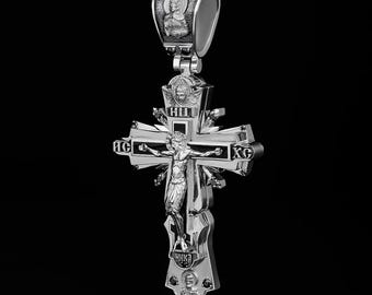 May include: A silver cross pendant with intricate details, featuring a depiction of Jesus Christ on the cross. The cross is adorned with black enamel and Cyrillic lettering.