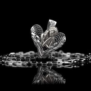 May include: A silver pendant necklace with a detailed angel figure within a heart-shaped frame. The angel has closed eyes and feathered wings. The necklace chain is visible below the pendant, set against a black background.