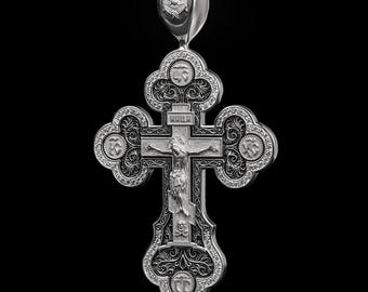 May include: A detailed silver pendant in the shape of a cross, featuring intricate carvings and religious iconography. The cross has a central figure of Jesus Christ and ornate floral and geometric patterns. The pendant is suspended from a loop at the top.
