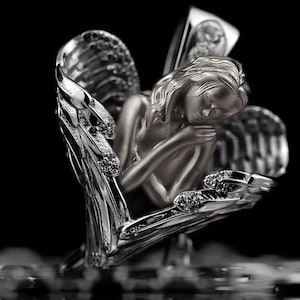 May include: A silver sculpture of an angel, with detailed wings and a serene expression. The angel is cradled within a heart-shaped structure, adorned with sparkling accents. The artwork is set against a dark background.