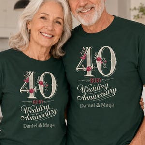 Op de afbeelding: Een stel draagt bijpassende donkergroene t-shirts ter ere van hun 40e huwelijksverjaardag. De shirts tonen het nummer "40" met bloemaccenten, de woorden "Ruby Wedding Anniversary" en de namen "Daniel & Maya".