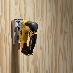 May include: A yellow and black DeWalt XR cordless jigsaw mounted on a white bracket against a wood-paneled wall. The tool is designed for cutting various materials. The image highlights the tool's design and brand.