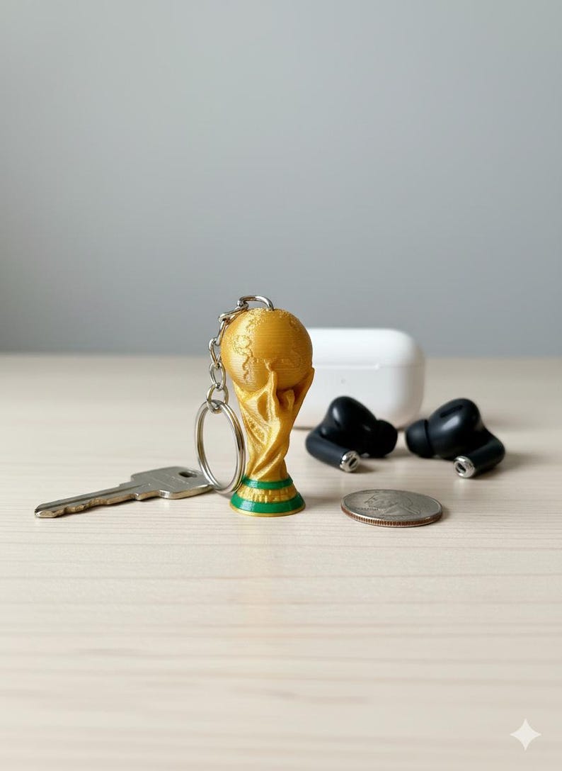 Pu&ograve; includere: Un portachiavi a forma di trofeo dorato con base verde, una chiave d'argento, una moneta e auricolari wireless neri. Sullo sfondo, una custodia di ricarica bianca.
