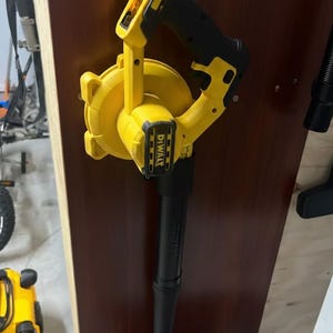 May include: A yellow and black cordless leaf blower with the brand name "DEWALT" visible. The blower has a black nozzle and handle, and is mounted on a wooden surface. The design is ergonomic and suitable for yard work.