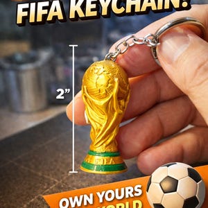 Pu&ograve; includere: Un portachiavi con trofeo della Coppa del Mondo FIFA dorato, alto 5 cm. Il portachiavi ha una base verde e una catena argentata. L'immagine include un pallone da calcio e il testo: "OWN YOURS MINI WORLD CUP TROPHY."