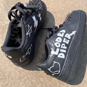 May include: Pair of black trainers with white graffiti-style designs and silver metal spikes on the top. The trainers have black laces and the words "LIVEDIE" and "Loded Diper" are written on the sides.