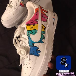 May include: White sneakers with colorful, dripped paint design on the side. The design includes shades of pink, orange, yellow, and blue. The Nike swoosh is white. The second sneaker has a tie-dye design on the side.