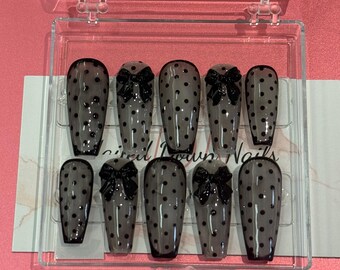 May include: A set of ten artificial nails in a clear plastic case. The nails are a sheer gray with black polka dots and black bow accents. The nails are in a coffin shape. The text "inspired brown nails" is visible on the packaging.