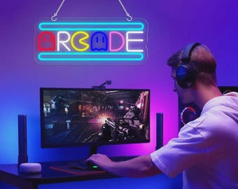 May include: A neon sign with the word "ARCADE" in red, yellow, and blue, with a ghost-like figure in the letter "A". The sign is hanging above a computer monitor. The scene is illuminated with blue and purple lighting, creating a gaming atmosphere.