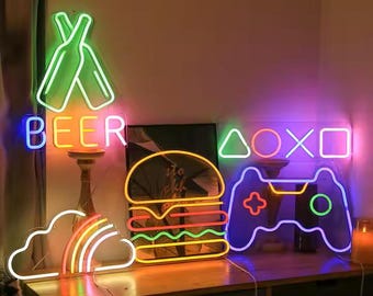 May include: A collection of neon signs in various shapes and colors. The signs include a pair of green beer bottles with the word "BEER" in blue, a rainbow, a burger, a game controller, and gaming symbols.