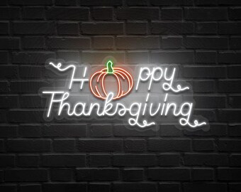May include: A neon sign on a dark brick wall displays the words "Happy Thanksgiving" in white cursive script. A pumpkin graphic with orange and green accents is centered above the word "Thanksgiving". The sign glows brightly.
