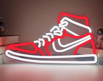 May include: A neon sign in the shape of a high-top sneaker. The sign features a red outline with white accents, including the laces and the Nike swoosh. The shoe is illuminated, creating a vibrant glow.