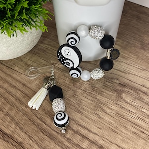 May include: A black and white beaded bracelet and keychain set. The bracelet features black, white, and rhinestone beads, with a yin-yang charm. The keychain has a tassel and coordinating beads.