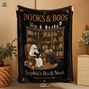 May include: A black rectangular throw blanket featuring the text BOOKS & BOOS at the top and Sophia's Book Nook at the bottom. The design shows a ghost reading in a chair, a black cat, a bookshelf, pumpkins, and skulls in orange and white.
