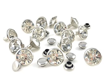 May include: A collection of silver-toned metal studs with clear crystal accents. The studs have a round, flat base and a raised, pointed top. The crystals are faceted and sparkle.