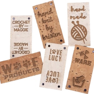May include: Eight cork fabric labels with various text and designs. The labels include "CROCHET - BY - MAGGIE", "hand knit by kristen", "LOVE LUCY", "W%%F PRODUCTS", "hand made", "WARE", and two labels with "LOVE LUCY" text.