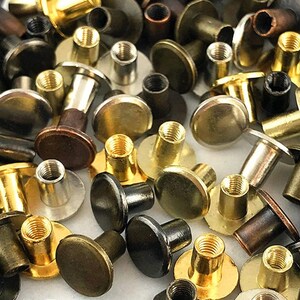 Chicago screws are shown in various colors offered, strewn across a white table. Colors include Silver, Gold, Bronze, Copper, Gray metal