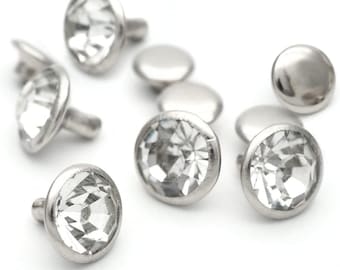 May include: A close-up of a group of silver-toned metal studs with clear crystal accents. The studs have a flat, round base and a small, pointed post.