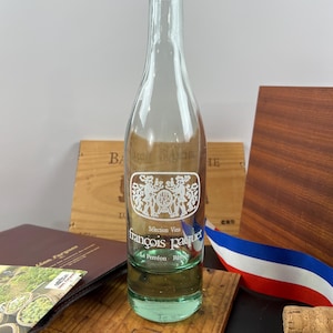 Puede incluir: Una botella de vino de vidrio transparente con un tinte verde en la parte inferior. La botella está etiquetada con el texto "Selection Vins Francois Paquet Le Perreon Rully".