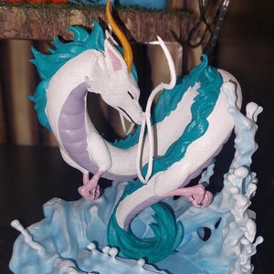 May include: A white and blue dragon figurine with a yellow horn, standing on a blue and white wave base. The dragon is curled up with its tail in its mouth.