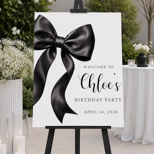 Op de afbeelding: Een wit rechthoekig bord op een zwarte ezel met een grote, glanzende zwarte satijnen strik aan de linkerkant. De tekst luidt: WELCOME TO Chloe's BIRTHDAY PARTY APRIL 14, 202X. Het ontwerp maakt gebruik van zwarte schreef- en scriptletters.