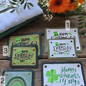 Peut inclure: Quatre patchs en tissu vert et blanc avec des trèfles brodés et le texte "Happy St. Patrick's Day". Les patchs sont sur une surface en bois avec une couverture verte et blanche en arrière-plan.