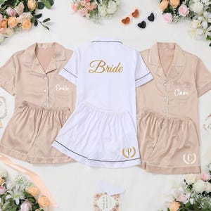 May include: Three sets of satin pajama sets. Two sets are a light tan color, and one is white. The white set has the word "Bride" in gold script on the back. The tan sets have names embroidered on the front pocket.