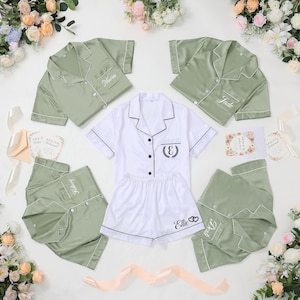 May include: Sage green and white pajama sets with personalized embroidery. The sets include button-down shirts and shorts or pants. The white set has a black embroidered initial and the name "Ellie". The green sets have names embroidered on the shirt.