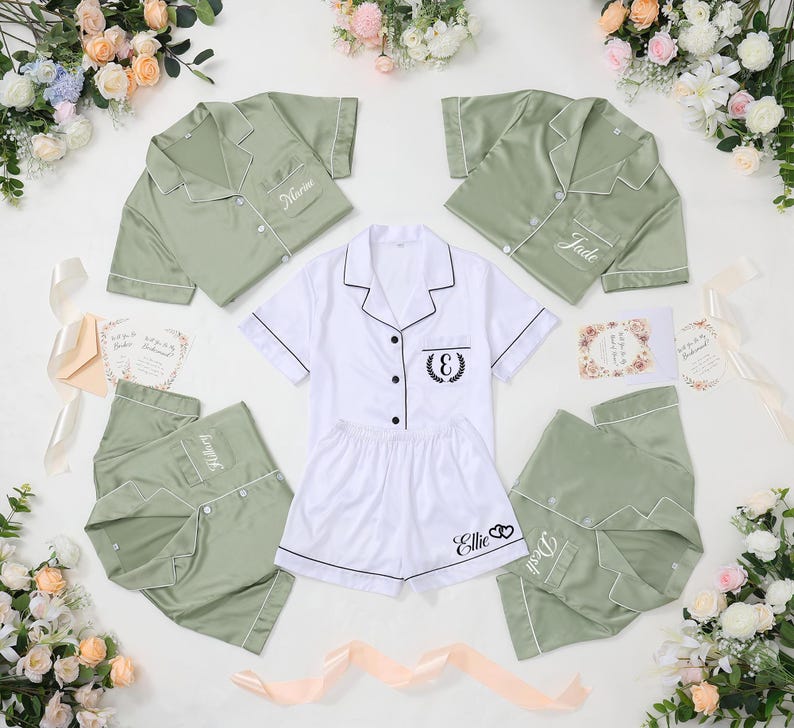 May include: Sage green and white pajama sets with personalized embroidery. The sets include button-down shirts and shorts or pants. The white set has a black embroidered initial and the name "Ellie". The green sets have names embroidered on the shirt.