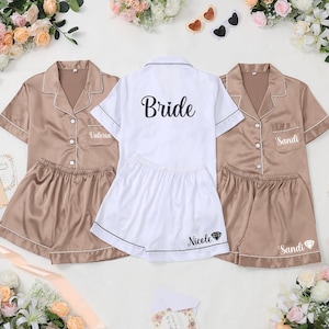 May include: Satin pajama sets in tan and white. The tan sets have the names "Valeria" and "Sandi" embroidered on the pocket. The white set says "Bride" on the back and "Nicole" on the shorts. All sets have white trim.