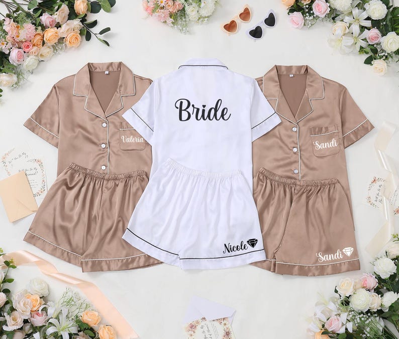 May include: Satin pajama sets in tan and white. The tan sets have the names "Valeria" and "Sandi" embroidered on the pocket. The white set says "Bride" on the back and "Nicole" on the shorts. All sets have white trim.