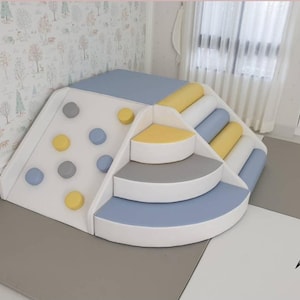 以下が含まれることがあります： 白、青、黄、グレーのマルチカラーのソフトプレイ構造。円形のグリップ、階段、スライド、丸みを帯びた柱を備えたクライミングウォールがあります。子供の遊びと発達のために設計されています。