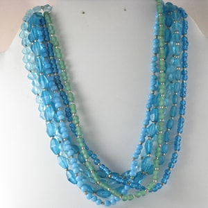 May include: Multi-strand necklace made of blue and green glass beads. The necklace is layered with different sizes and shapes of beads.