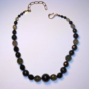 May include: A black and green beaded necklace with a gold chain and clasp.