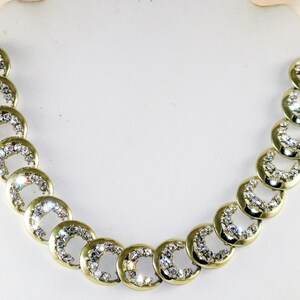 May include: A gold necklace with a chain made of linked circles, each circle is encrusted with clear rhinestones.