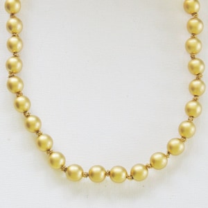 May include: A gold-colored necklace featuring a series of round beads. The beads have a matte finish and are strung together with a delicate chain and clasp. The necklace is displayed against a white background.