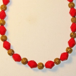 May include: A red and gold beaded necklace with a gold clasp. The beads are faceted and have a geometric shape.
