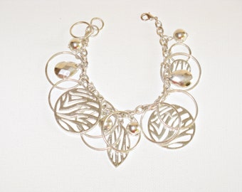 May include: Silver charm bracelet with multiple circular and leaf-shaped charms. The bracelet has a chain link design.