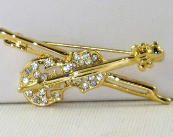 May include: A gold-toned violin brooch with a bow, adorned with clear rhinestones. The brooch is a musical instrument-themed accessory, perfect for musicians or those who appreciate music. The violin is approximately 2 inches long.
