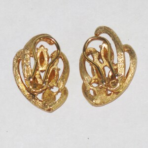 May include: A pair of gold-tone clip-on earrings with a swirl design and clear rhinestones. The earrings are marked "BSKO" on the back.