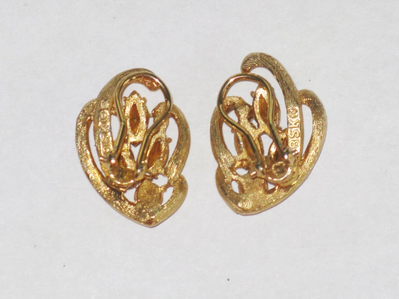May include: A pair of gold-tone clip-on earrings with a swirl design and clear rhinestones. The earrings are marked "BSKO" on the back.