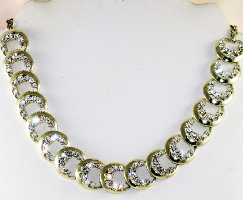 May include: A gold necklace with a chain made of linked circles, each circle is encrusted with clear rhinestones.