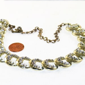 May include: A gold tone necklace with a chain and a series of linked, crescent-shaped charms set with clear rhinestones.